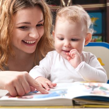 Woman pointing out a page in a book to a young toddler